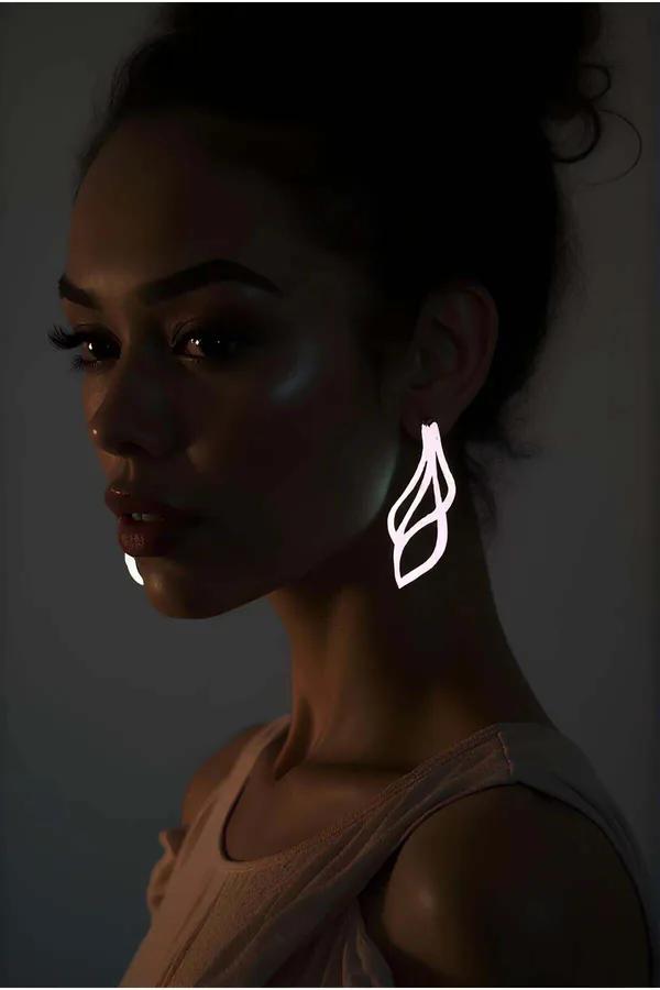 White reflective laser-cut abstract swirl dangle earrings glowing in low-light worn on model