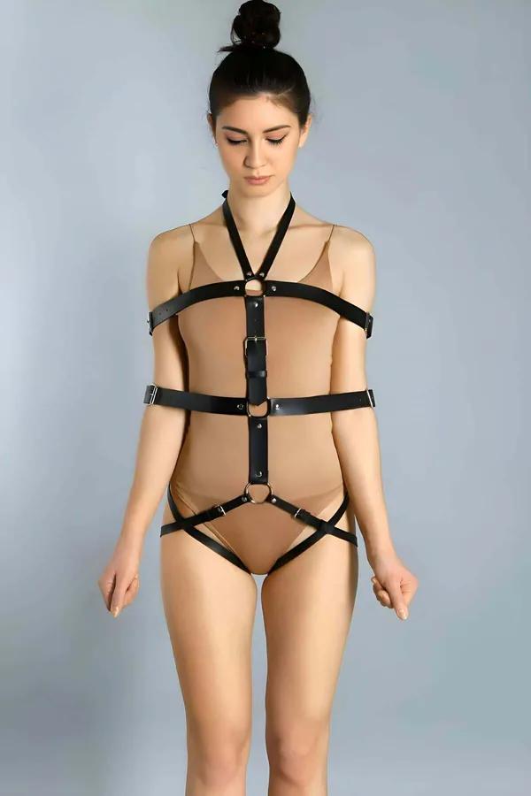 Black faux leather full body harness with three silver O-rings on center spine and detachable chain, worn as fashion layering