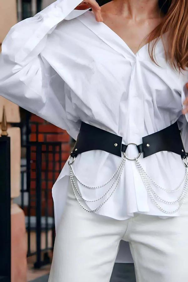 Black wide faux leather waist harness belt with silver O-ring center and layered chain drapes worn over white shirt