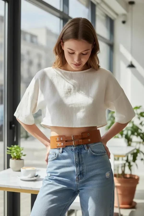 wide tan faux leather waist belt with three silver buckles worn over jeans and white crop top