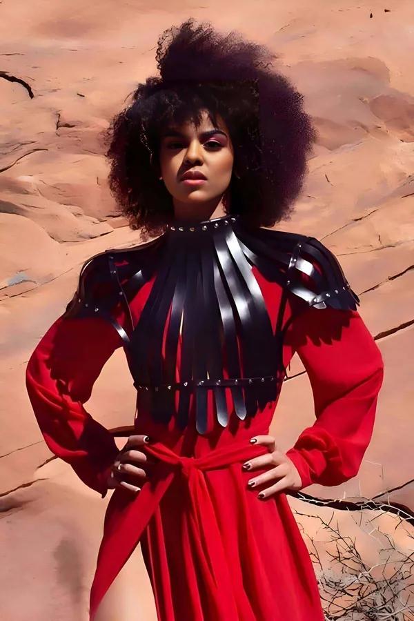 black faux leather shoulder harness with vertical fringe strips and silver studs worn over red dress