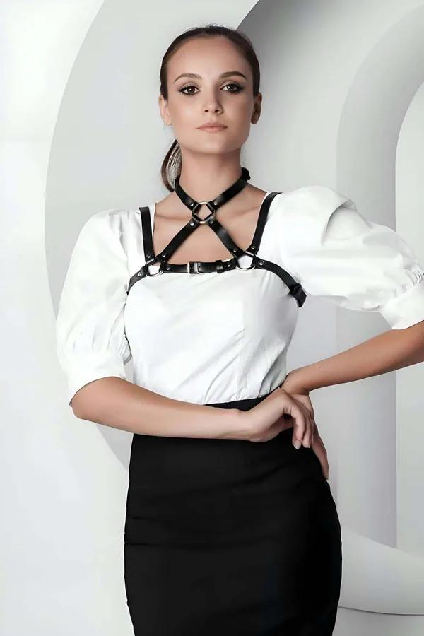 Black faux leather chest harness with dual O-rings and silver buckles worn over white blouse