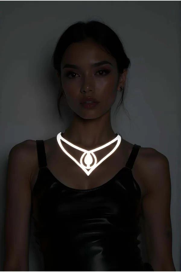 Reflective silver geometric V-wing choker with teardrop drop pendant glowing white under low light on model