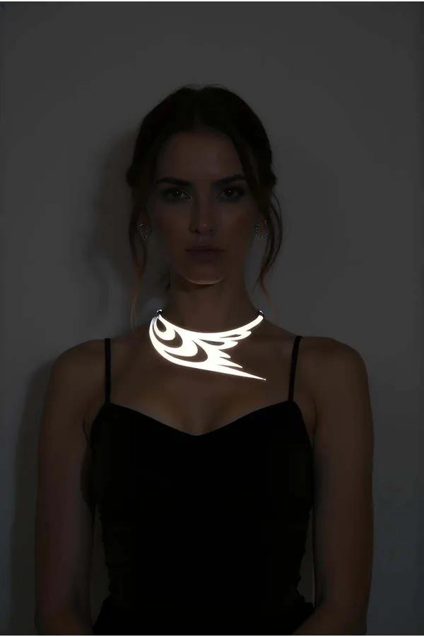Silver reflective laser-cut choker necklace with tribal wing cutout design glowing white under direct light