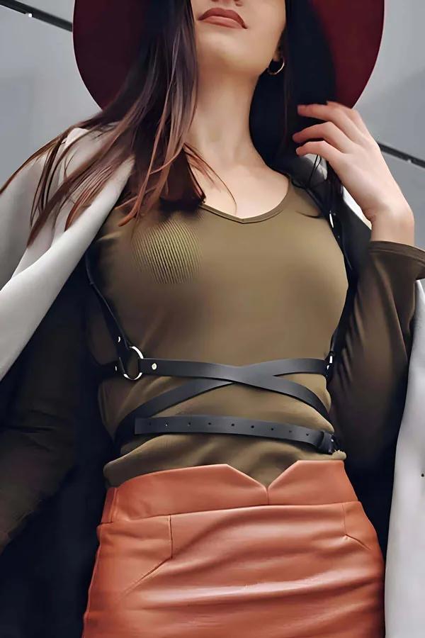 Black faux leather crisscross chest harness with silver O-ring worn over olive ribbed top and terracotta mini skirt