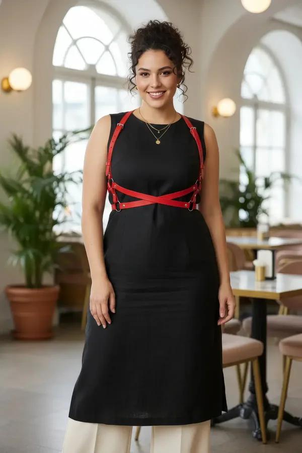Red faux leather cross-chest harness with gold O-rings and X-strap design worn over black dress