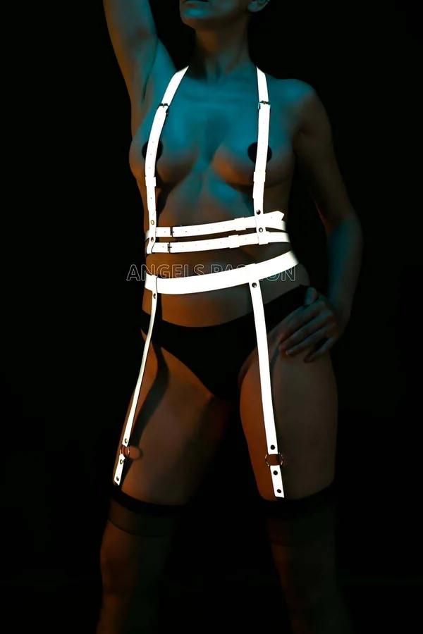 White reflective body harness with four garter straps and bronze O-ring hardware glowing under dark lighting