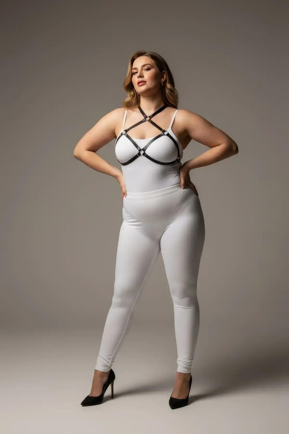 Black faux leather O-ring chest harness with silver hardware crossing straps over white bodysuit