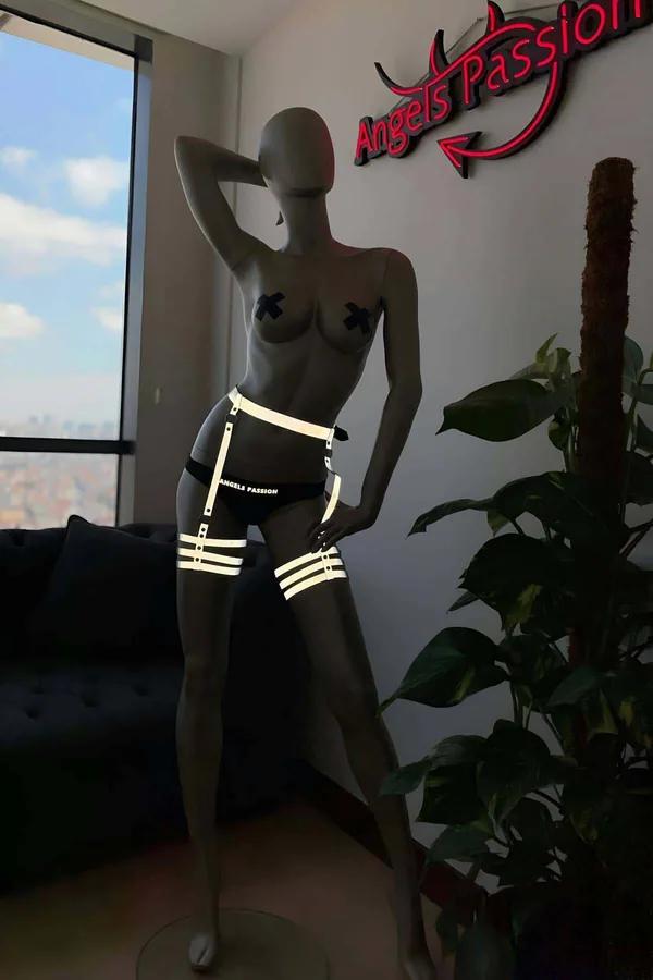 Black reflective leg harness garter with three adjustable thigh straps and silver buckles glowing under direct light