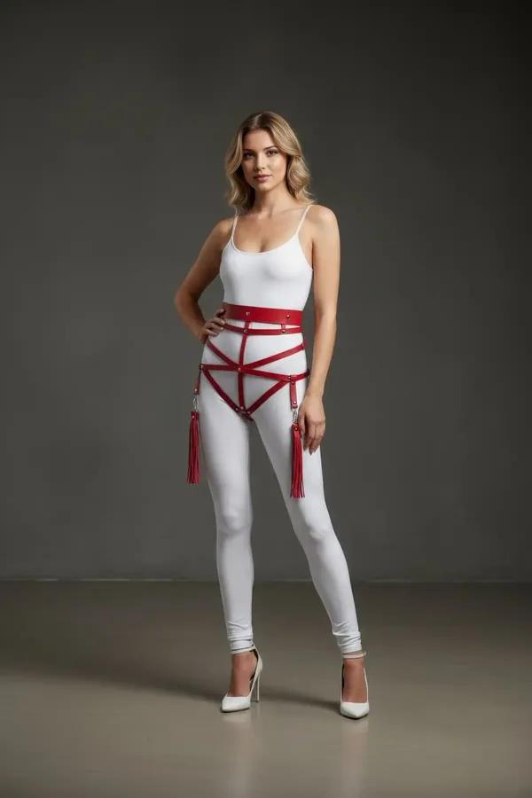 Red faux leather high-waist hip harness with geometric cage straps, silver O-rings, and detachable red tassels worn over whit
