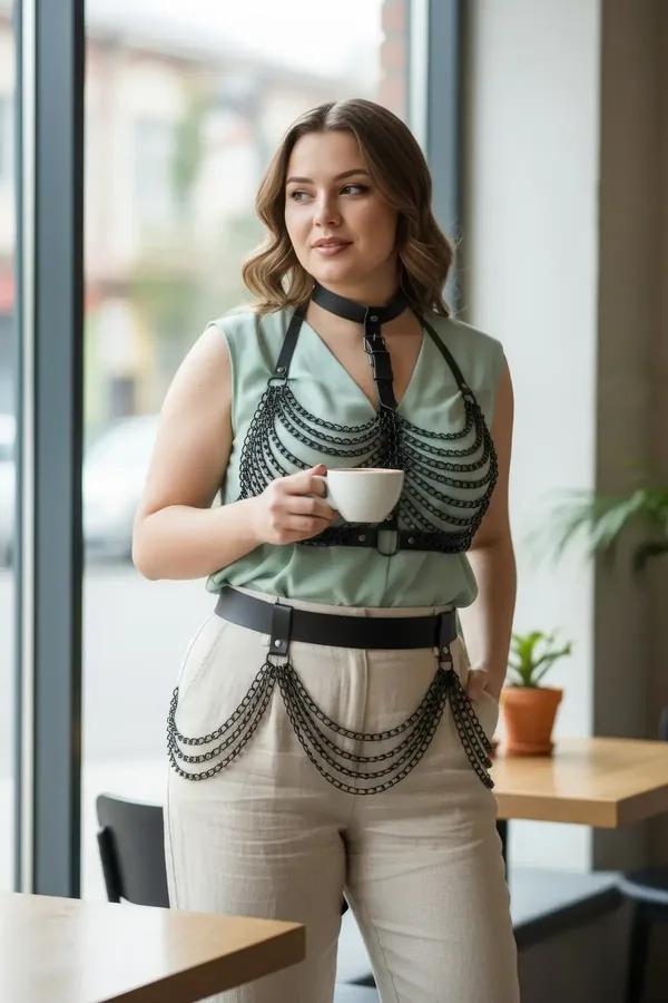 black faux leather full body harness with draped chain overlay on chest and wide waist belt with chain swags worn over sage g