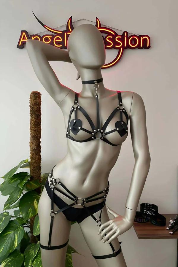 Black faux leather full body harness set with heart pasties, silver O-rings, choker collar and thigh garter bands on mannequi