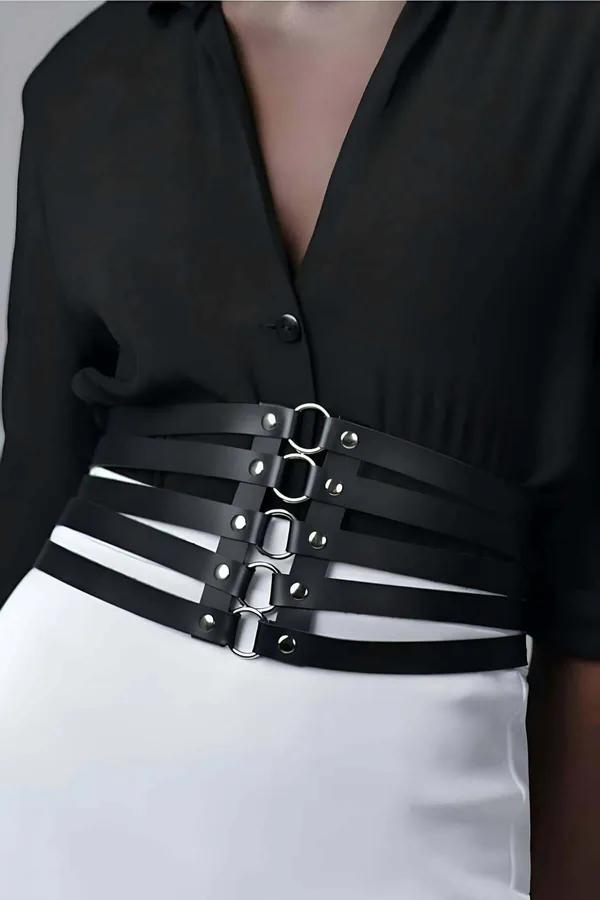 black faux leather strappy waist harness with five horizontal straps and silver O-ring hardware worn over black blouse and wh