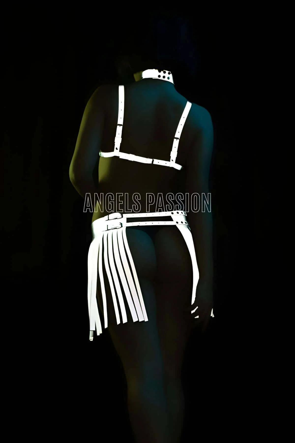 Long white faux leather fringe strips on harness top shoulders catching direct light against dark background