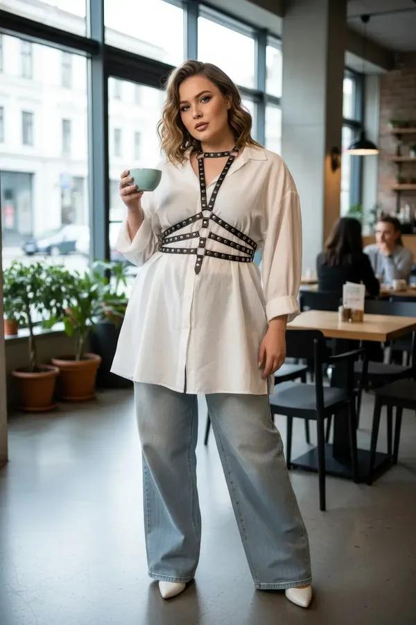 Black faux leather chest harness with silver rivets and O-ring detail layered over a white oversized shirt