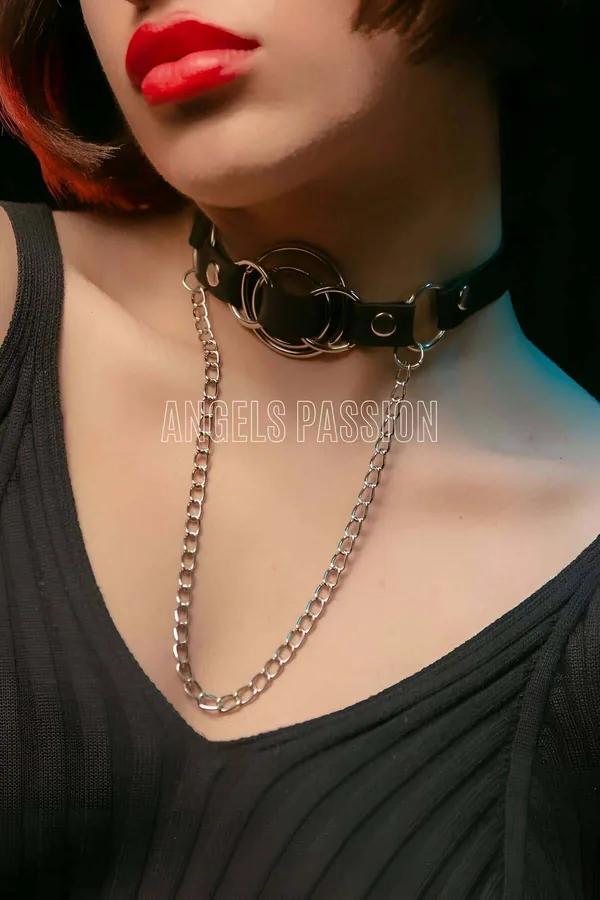 Black faux leather choker with triple silver O-rings and draped curb chain worn around neck
