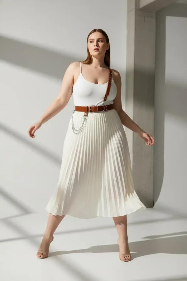 tan faux leather single shoulder harness belt with silver chain detail worn over white bodysuit and pleated skirt