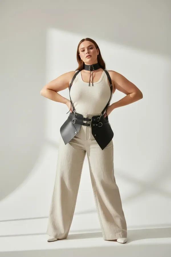 Black faux leather integrated choker body harness with angular waist panels and silver O-ring hardware worn over cream tank t