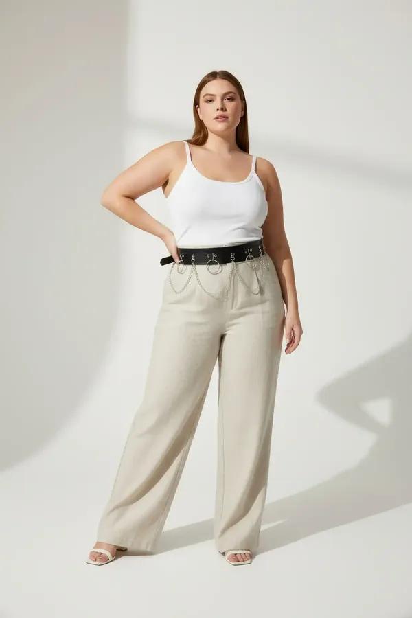 Black faux leather harness belt with five silver O-rings and draped chains worn over wide-leg beige trousers