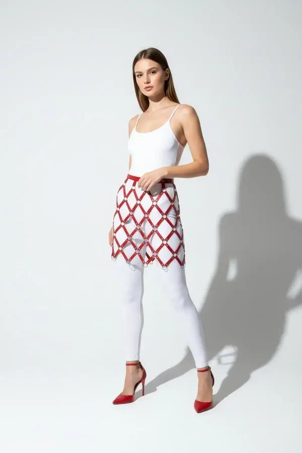 Red and white argyle faux leather waist harness skirt with silver O-ring intersections worn over white leggings