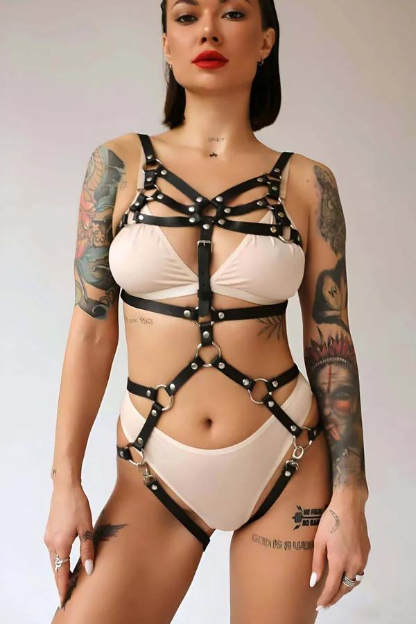 Black faux leather full body harness with silver O-rings and dome studs worn over nude lingerie, front view