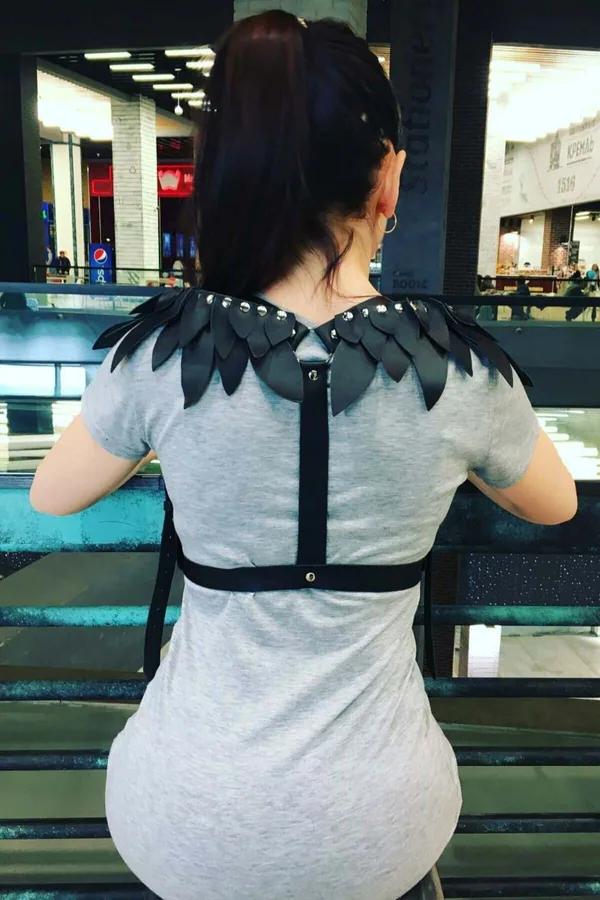 Black faux leather winged shoulder harness with silver dome studs and adjustable back strap worn over gray t-shirt
