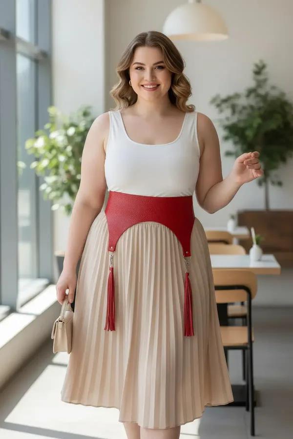 Red wide faux leather waist belt harness with dangling red tassels worn over white top and beige pleated skirt