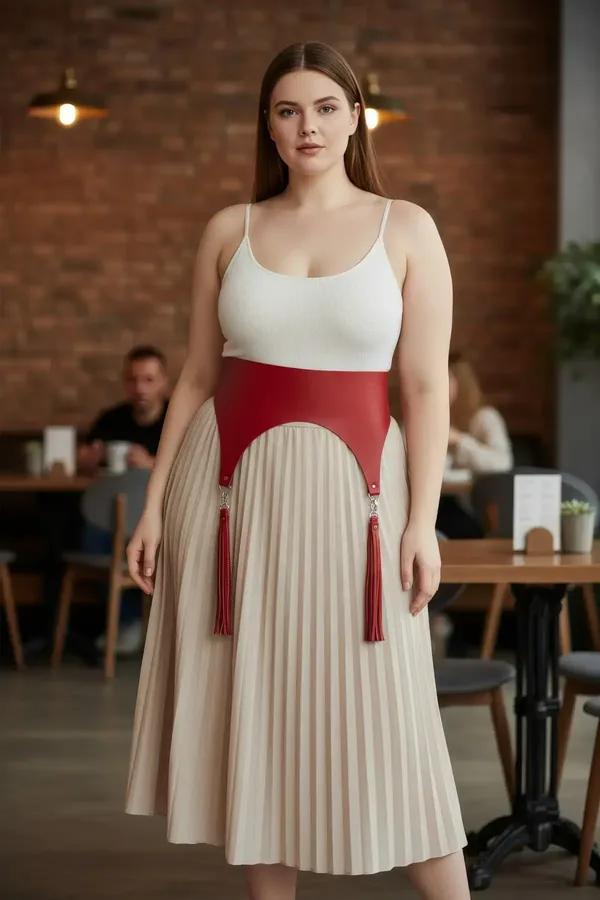 Red vegan leather waist harness with detachable tassels worn over white top and beige pleated midi skirt, silver hardware cli