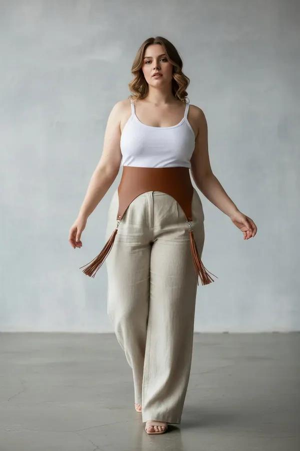 Tan faux leather wide waist harness with fringe tassel garter straps and silver clip hardware worn over wide-leg trousers