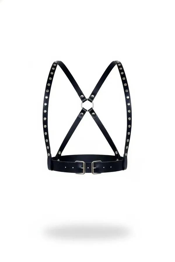 Black faux leather chest harness with silver dome studs along X-back straps, central O-ring, and dual rectangular buckles at 