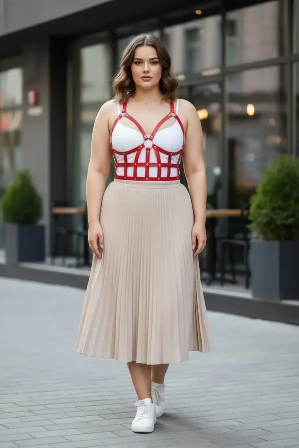 Red faux leather caged bustier harness with silver rivets worn over white bra and beige pleated skirt