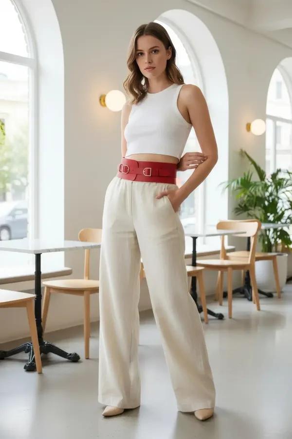 red faux leather wide waist cincher harness with two silver rectangular buckles worn over white crop top and cream trousers