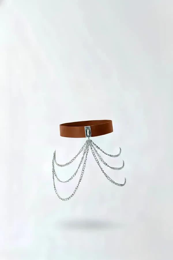 Tan faux leather waist harness with four draped silver chain strands and rectangular center clasp, front view