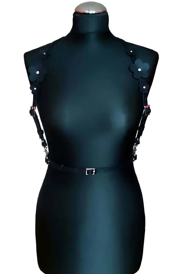 black faux leather chest harness with large flower appliqués at shoulders and silver rectangular waist buckle on mannequin
