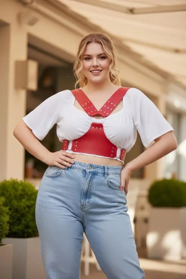 Red faux leather chest harness with gold stud rows and front O-ring worn over white t-shirt with jeans