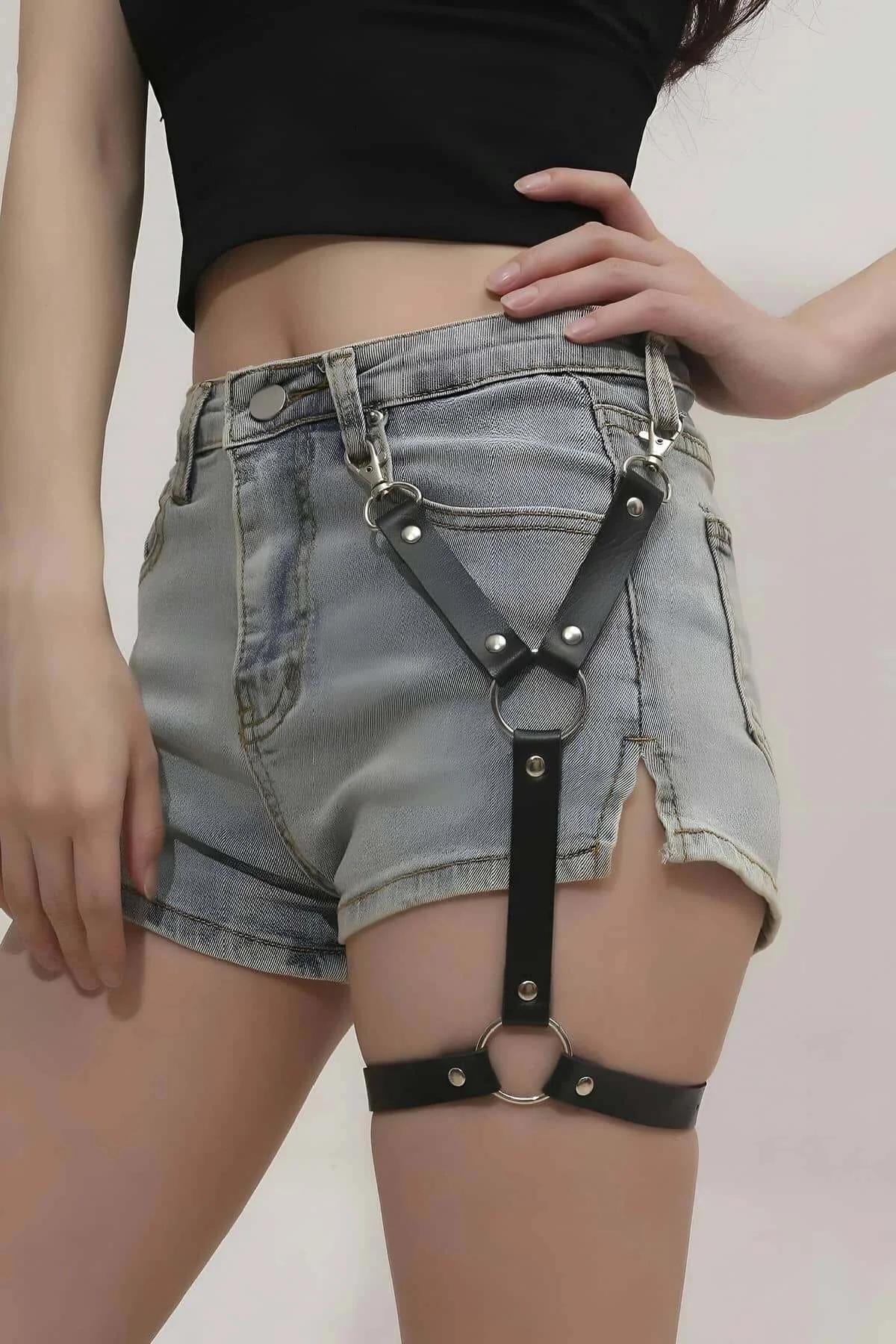 Black faux leather leg garter harness with silver O-rings clipped to denim shorts belt loops and thigh band