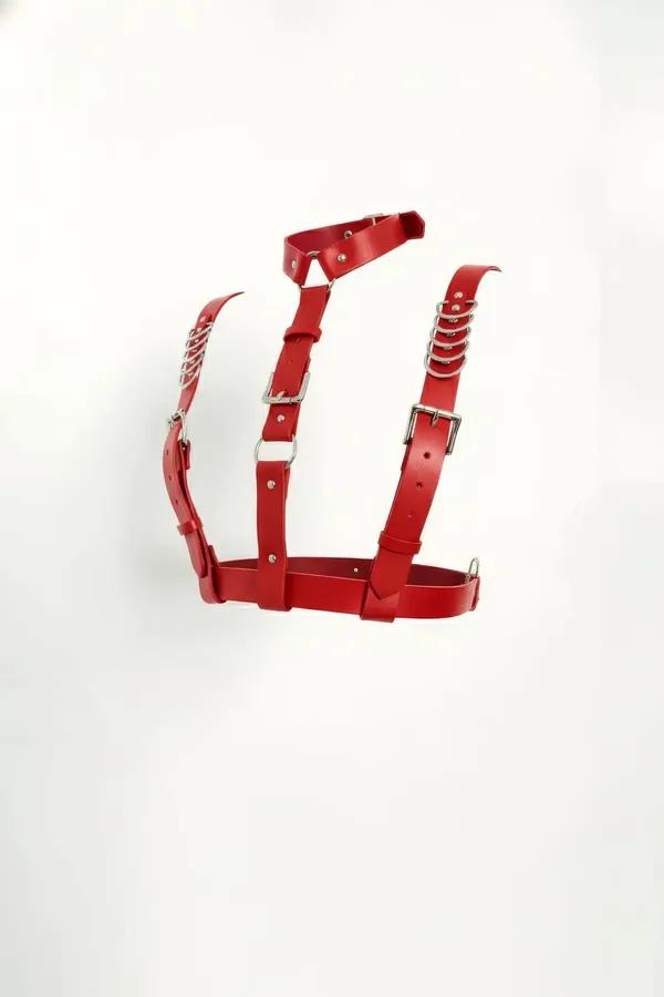 Red faux leather chest harness with stacked silver O-rings and adjustable rectangular buckles on white background