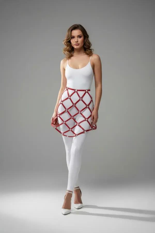 Red faux leather lattice skirt harness with silver stud intersections worn over white leggings and bodysuit
