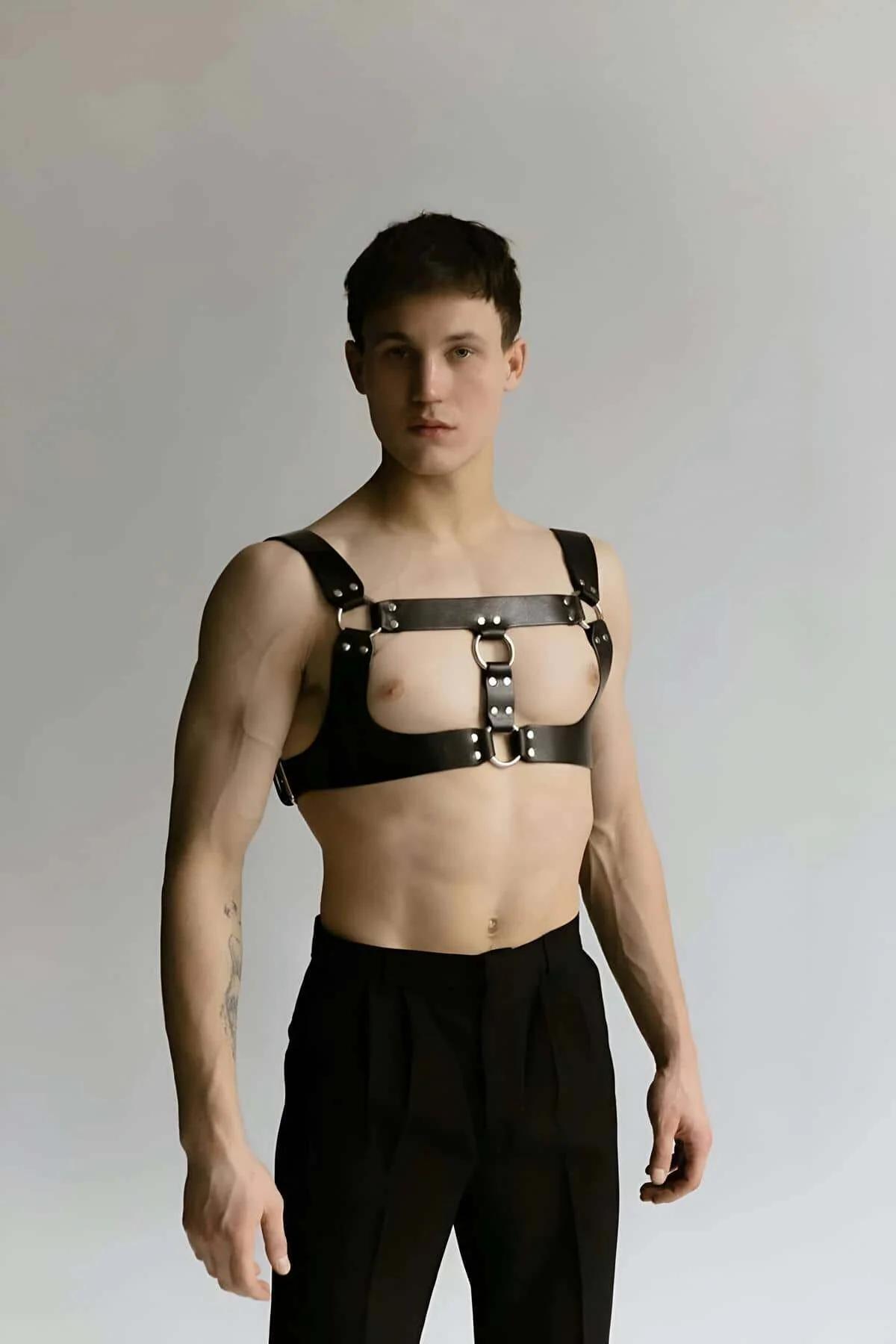 Brown fashion harness with polished silver O-rings styled over bare torso with black trousers