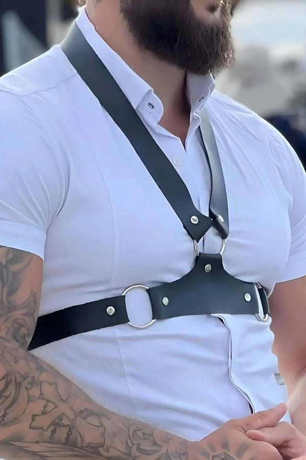 Black faux leather cross-chest harness with silver O-ring worn over white shirt, asymmetric diagonal strap and wide waistband