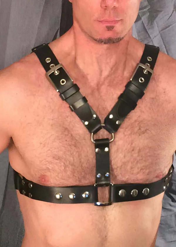 Black faux leather chest harness with silver buckles and dome rivets, Y-strap design with center D-ring, worn by a man