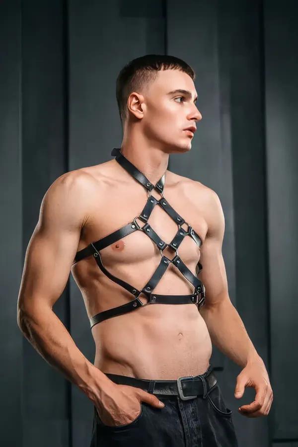Black faux leather cage chest harness with diagonal cross-straps, riveted O-rings, and collar band on male model