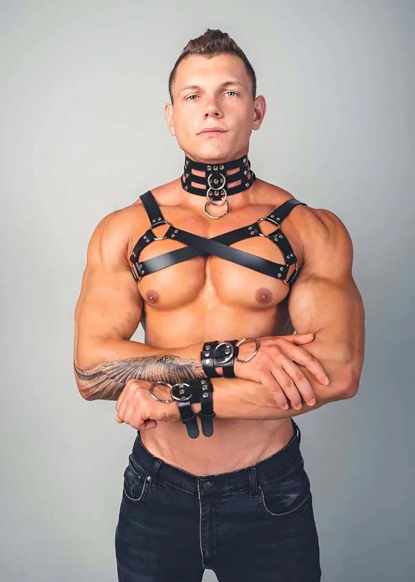 Black faux leather X-cross chest harness with wide studded collar and wrist cuffs on male model