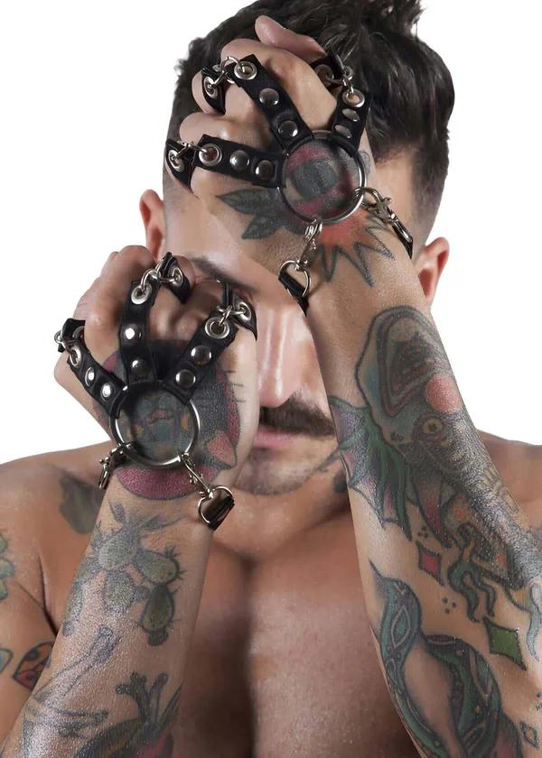 Black faux leather hand harness with silver O-ring at palm and dangling heart charm on tattooed male model