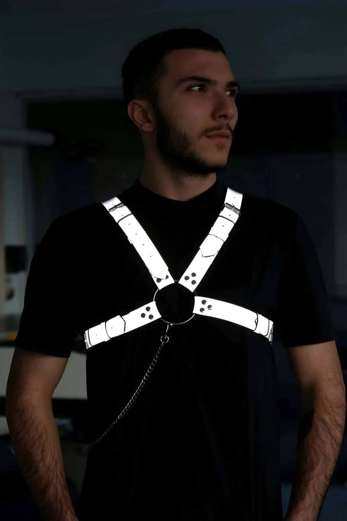 Reflective white chest harness with black O-ring center and chain detail worn by man over black t-shirt