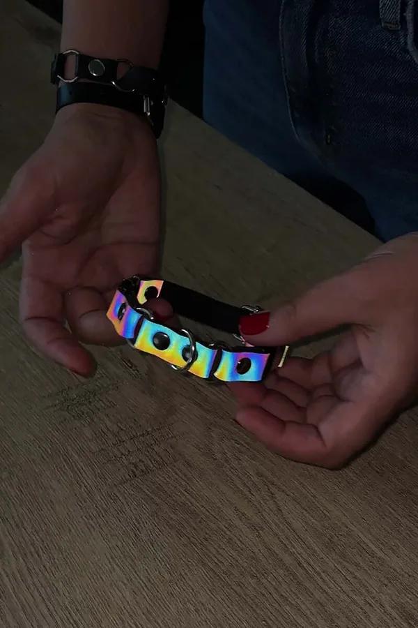 Reflective rainbow holographic choker with silver O-ring eyelets and black faux leather backing held in hands