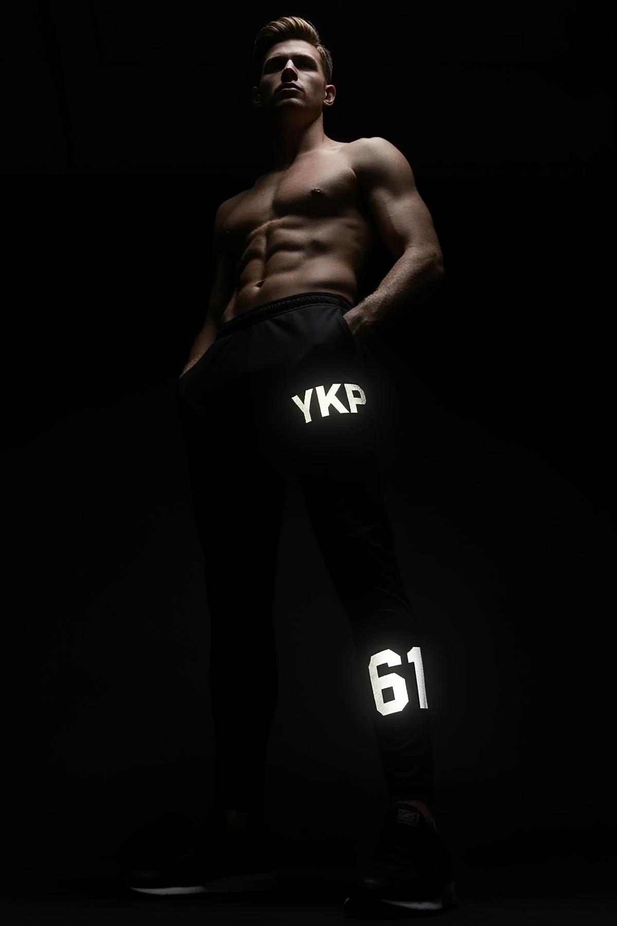 black reflective sport joggers with white MRT logo on thigh and number 98 near ankle hem glowing under light