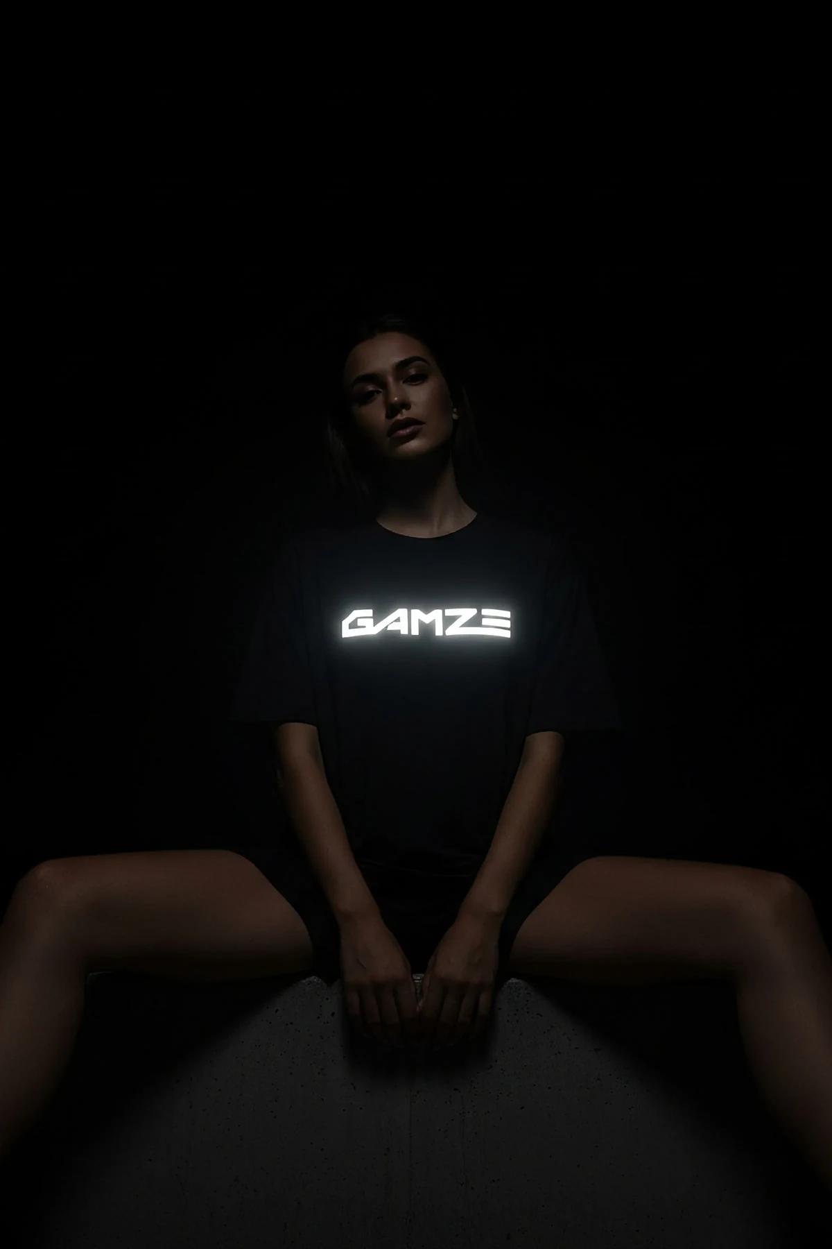 black reflective graphic t-shirt with bold custom text glowing bright white on chest in low-light studio shot