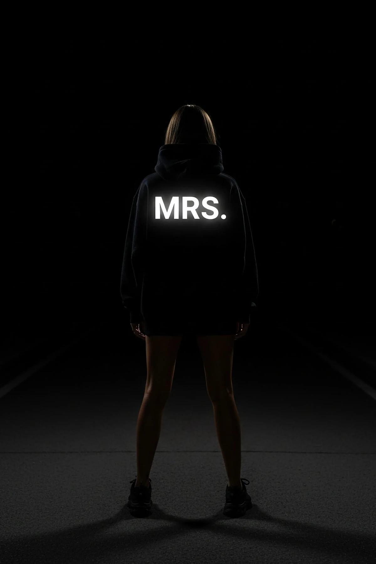 black oversized Mrs. hoodie with white reflective glow-in-the-dark MRS. block-letter sleeve print photographed at night