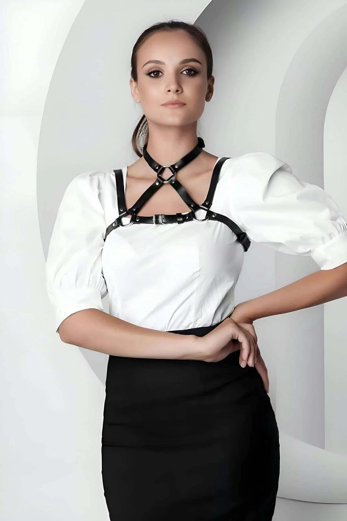Black faux leather chest harness with dual O-rings and silver buckles worn over white blouse